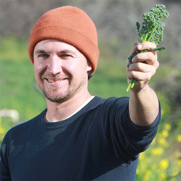 photo of an organic farmer in the field holding up a stalk of brocolli